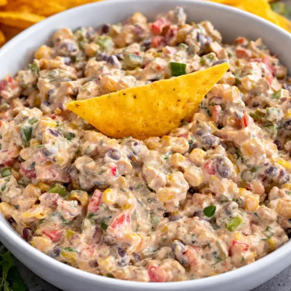 Bowl of creamy cowboy caviar dip with tortilla chips and fresh vegetables.