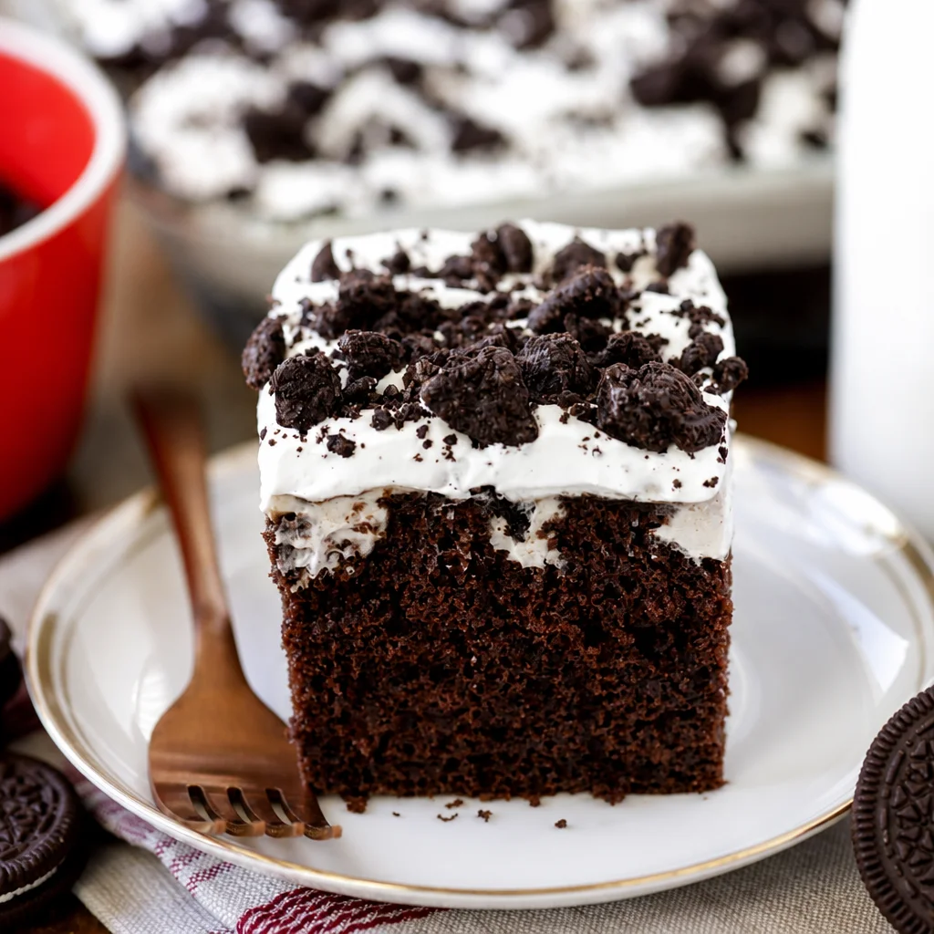 Slice of Easy Oreo Poke Cake topped with whipped cream and crushed Oreos
